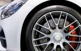 A close-up of the front right wheel well on a white sports car. The wheel features alloy rims and red brake calipers.