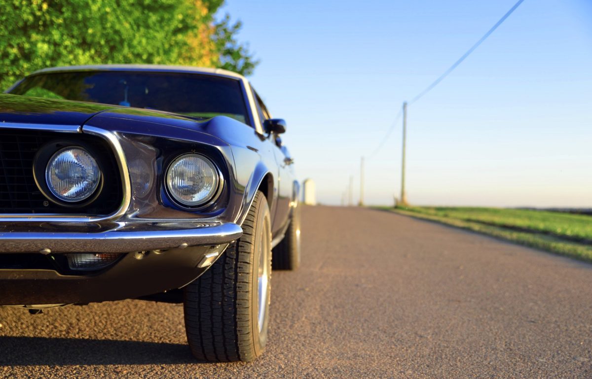 A close-up of a black-and-white vintage Mustang car. The vehicle is parked on the side of the road in a rural area.