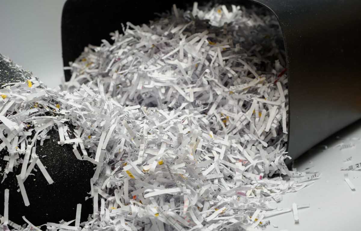 A paper shredder trash container is tipped over, allowing a huge pile of crosscut paper shreds to spill out.