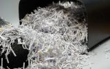 A paper shredder trash container is tipped over, allowing a huge pile of crosscut paper shreds to spill out.