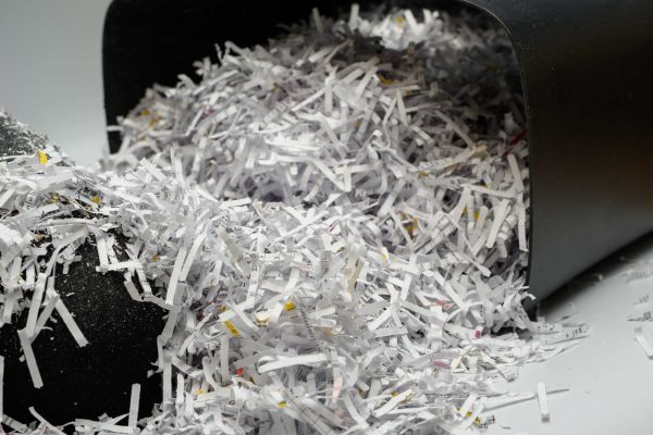 A paper shredder trash container is tipped over, allowing a huge pile of crosscut paper shreds to spill out.