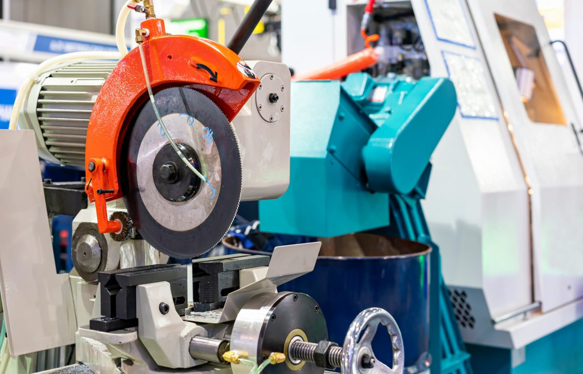 An industrial cold saw sitting on a commercial-grade work bench. The saw has an orange protector over it.