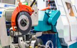 An industrial cold saw sitting on a commercial-grade work bench. The saw has an orange protector over it.