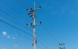 Two electricity posts are connected by running black cables. The background is a blue sky with small clouds on the left side.