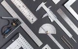 Aerial view of multiple metal measuring instruments laid next to each other on top of a flat gray surface.