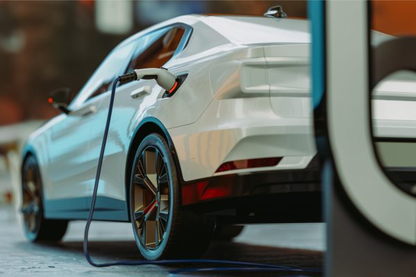 The back of a shiny white electric vehicle parked and hooked up to a charging station in a parking lot.