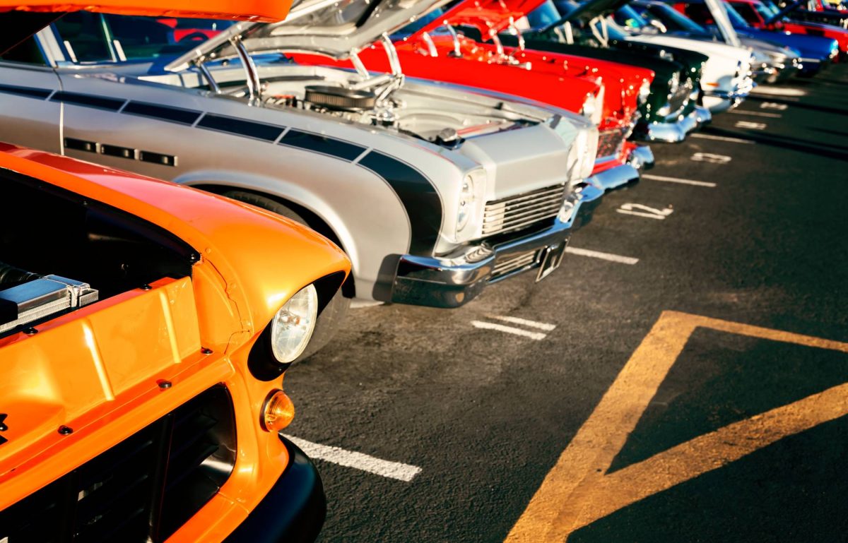 A close-up of a row of cars in various colors with their hoods up to show off the engines at a classic car show.