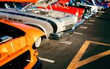 A close-up of a row of cars in various colors with their hoods up to show off the engines at a classic car show.