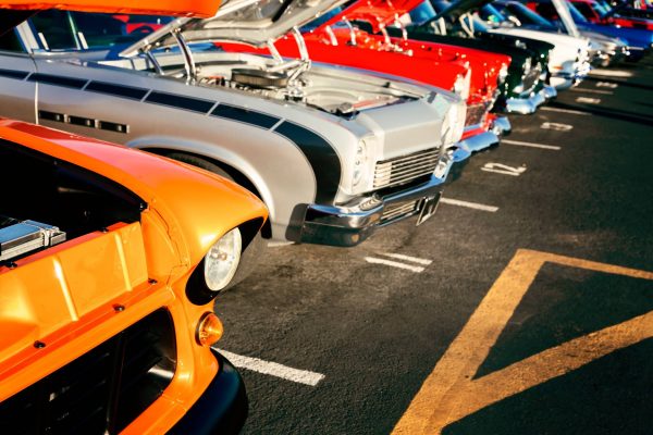 A close-up of a row of cars in various colors with their hoods up to show off the engines at a classic car show.