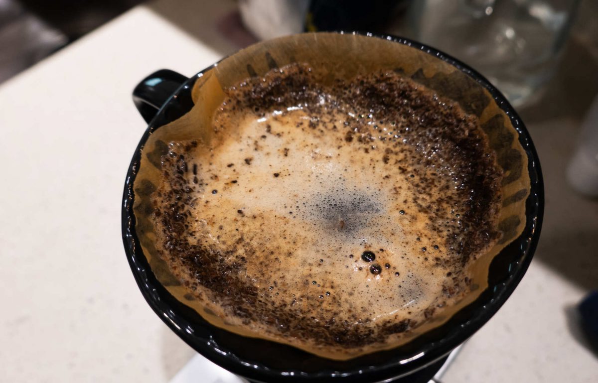 A pour-over coffee funnel with a filter and grounds sitting in the filter. There is water resting on the surface.