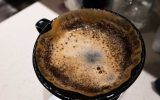 A pour-over coffee funnel with a filter and grounds sitting in the filter. There is water resting on the surface.