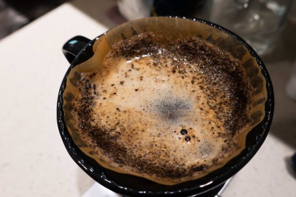 A pour-over coffee funnel with a filter and grounds sitting in the filter. There is water resting on the surface.