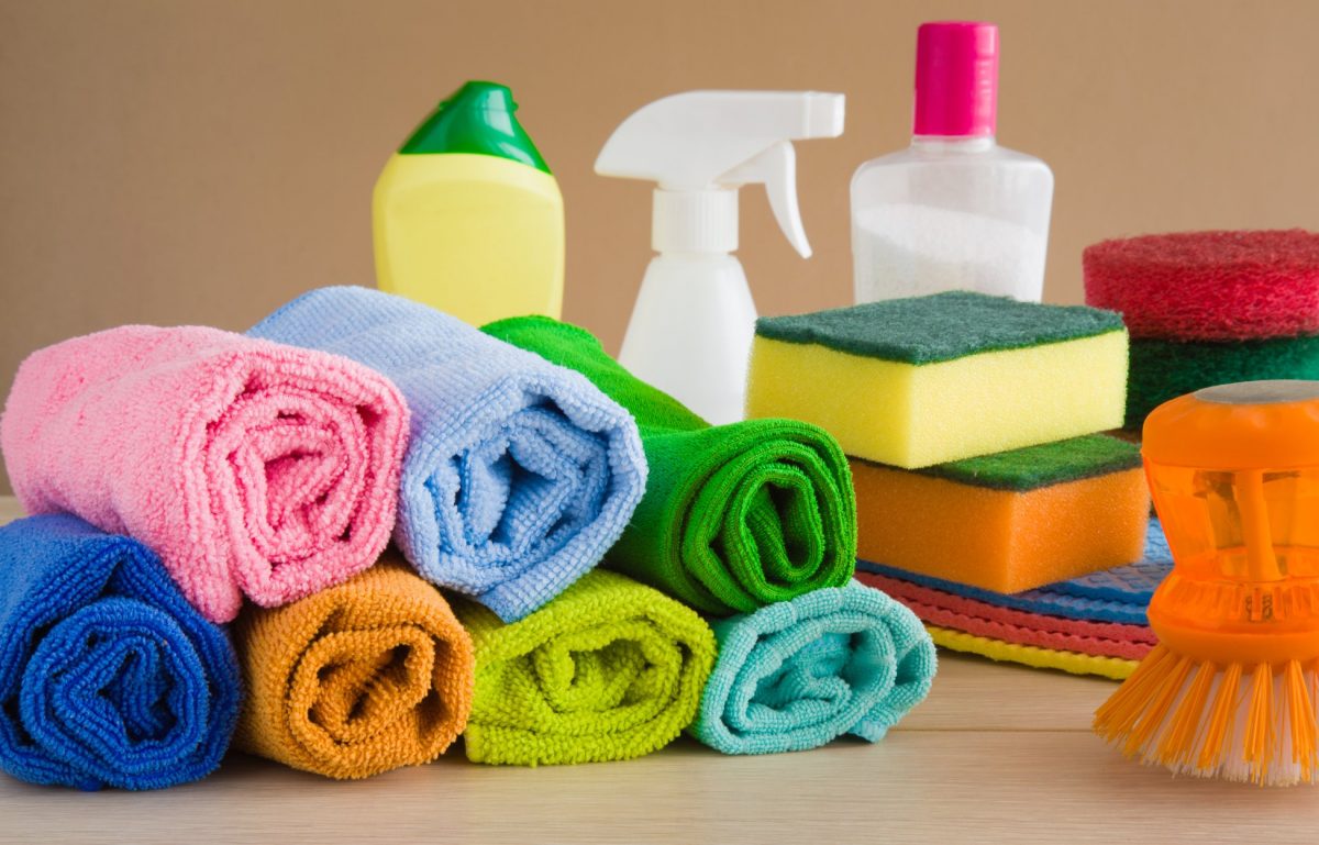 A pile of colorful microfiber towels rolled up next to other cleaning supplies, such as sponges and a spray bottle.