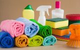 A pile of colorful microfiber towels rolled up next to other cleaning supplies, such as sponges and a spray bottle.