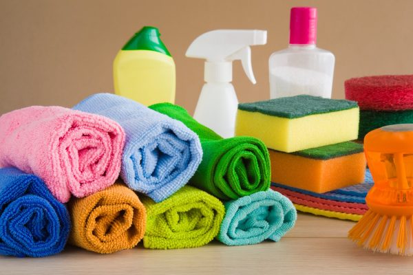 A pile of colorful microfiber towels rolled up next to other cleaning supplies, such as sponges and a spray bottle.