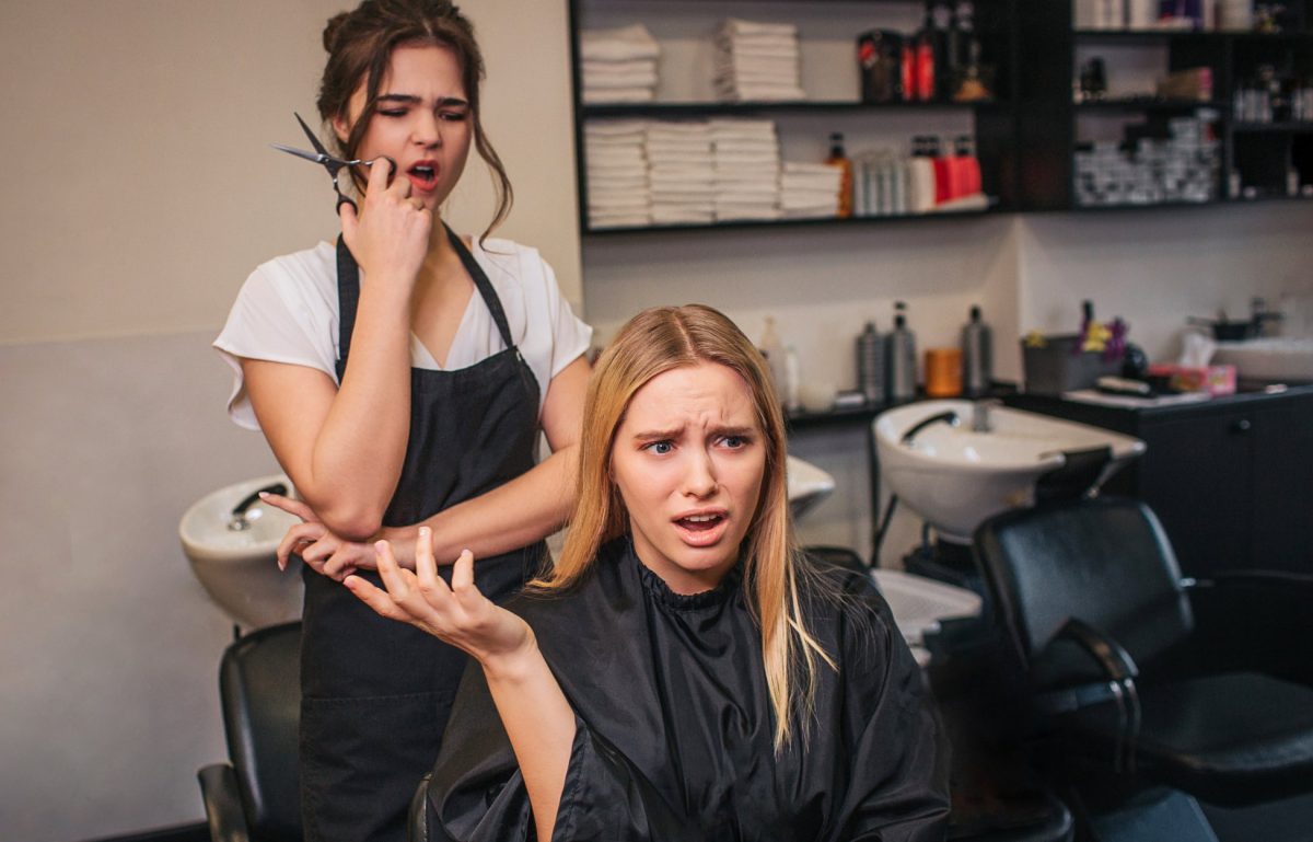 An upset salon client in a chair gestures angrily as her concerned stylist stands behind her with hair clippers.