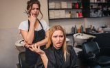 An upset salon client in a chair gestures angrily as her concerned stylist stands behind her with hair clippers.