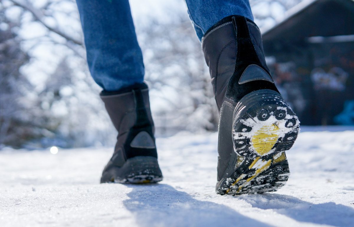 A person walking through the snow outside with a close-up shot of the soles of their black fur-lined boots.