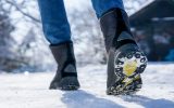 A person walking through the snow outside with a close-up shot of the soles of their black fur-lined boots.