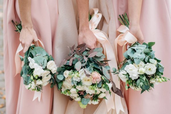 Three bridesmaids in light pink dresses stand together and hold large wedding bouquets of white flowers.