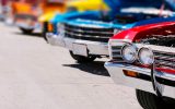 A lineup of classic cars of many different colors. The cars all have their hoods open.